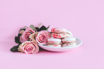 Tasty french macaroons with pink roses on a pink pastel background.