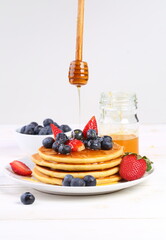 Still life with pancakes, berries and honey on a white background