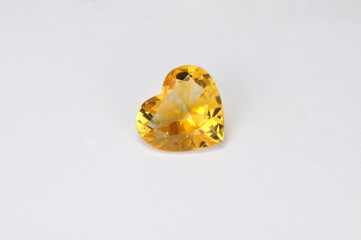 Natural yellow citrine heart shaped loose faceted gemstone on white background. Shiny polished stone quartz group mineral gradient zoned color pattern. Photo for articles on the topic of gemology.