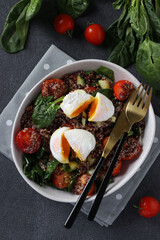 Salad with quinoa, spinach, poached eggs and cherry tomatoes in a plate on gray background. Healthy eating.