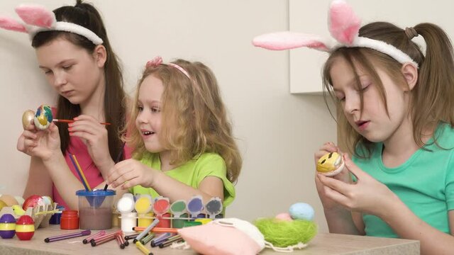 Three girls friends decorate with paint and brushes chicken eggs. Easter holiday. 4k video.