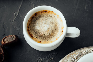 freshly brewed coffee with foam in small porcelain cupand dried dates in dark atmosphere. shot of caffeine for boost of energy. mug of hot breakfast drink. selective focus