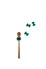 Bamboo spoon and Green pasta farfalle with spirulina on white background. Colored pasta with natural food dyes of organic origin