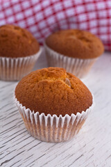 Morning breakfast vanilla muffins in white paper cups on a white wooden cutting board, white background, close-up view 