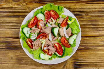Tasty tuna salad with lettuce and fresh vegetables on wooden table. Top view