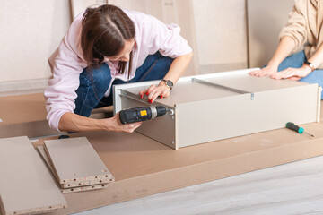 Women gather furniture together in the living room screw using electric screwdriver.