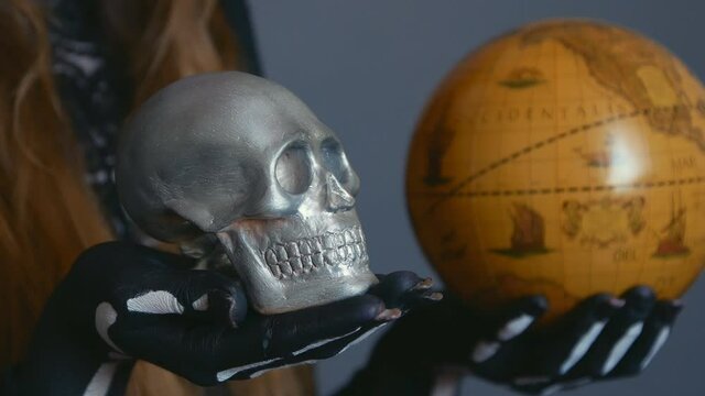 close-up of hands holding a globe and a skull. hands of a woman in the image of death Santa Muerte or sugar mexican.