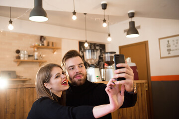 Smiling Woman And Handsome Man Drinking Coffee, Using Mobile Phone While Spending Time In A Coffee Shop.