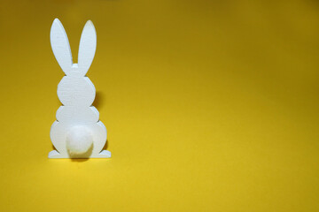 a white wooden figurine of an Easter bunny with a white tail stands on a yellow background, side view . Easter holiday