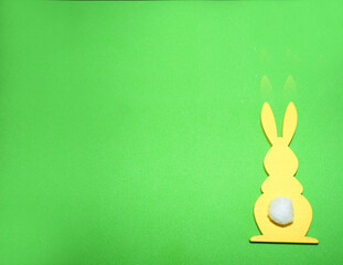 yellow wooden figurine of an Easter bunny with a white tail on a green background top view . Easter holiday