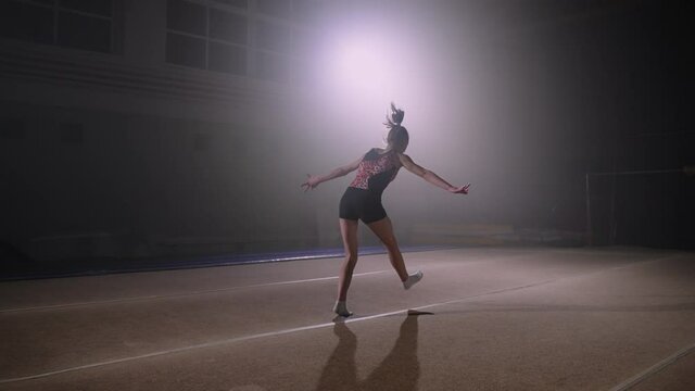 sporty teenage girl is performing somersault on spring floor, training alone, artistic gymnastics, slow motion shot