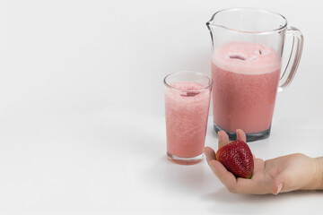 Concepto aislado de jugo de fresa en leche sobre una mesa blanca y una mano con una gran fresa sobre ella