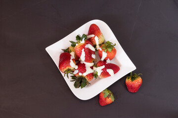 Concepto aislado de plato blanco de fresa sobre la mesa bañada en crema de leche en vista superior sobre fondo negro