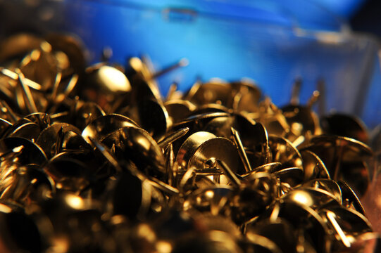 Golden metal push tacks in a plastic box, illustrating standard office and classroom supplies used for pinning materials to bulletin boards and display surfaces