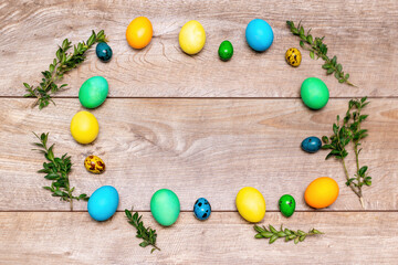Colorful easter chicken and quail eggs frame with green plant branches on wooden rustic background with copy space, spring easter concept, top view
