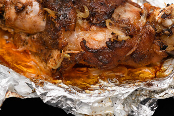 baked meat and fried onions on a baking sheet, pork ham on foil and wooden background, home cooking