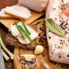 raw pork meat and lard with salt, spices and garlic on a cutting board, dark wooden background