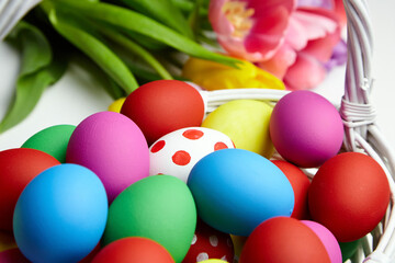 Easter eggs in basket and spring colorful flowers on white wooden table