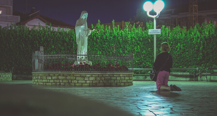 Unknown woman is praying in Medjugorje holy area during the night time.