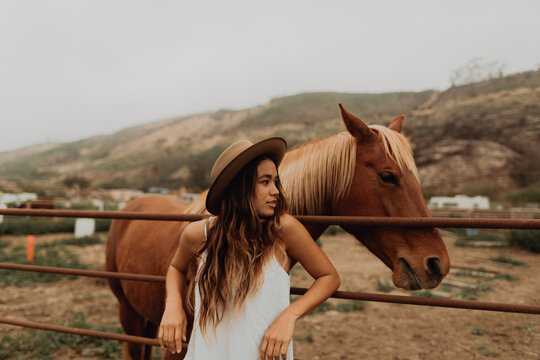 Young woman in felt hat leaning against fence next to horse, Jalama, California, USA
