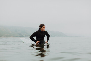 Young male surfer sitting on surfboard in calm misty sea, Ventura, California, USA