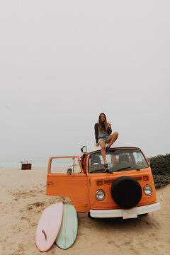 Young female surfer sitting on recreational vehicle roof at beach, portrait, Jalama, California, USA