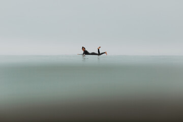 Young female surfer lying on surfboard in calm misty sea, full length portrait, Ventura, California, USA