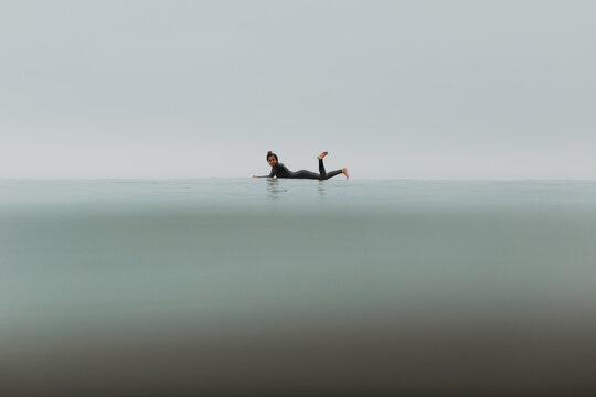 Young female surfer lying on surfboard in calm misty sea, full length portrait, Ventura, California, USA