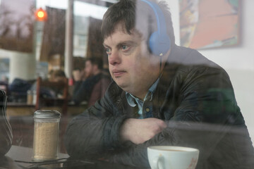 Man with down syndrome using headphones by cafe window