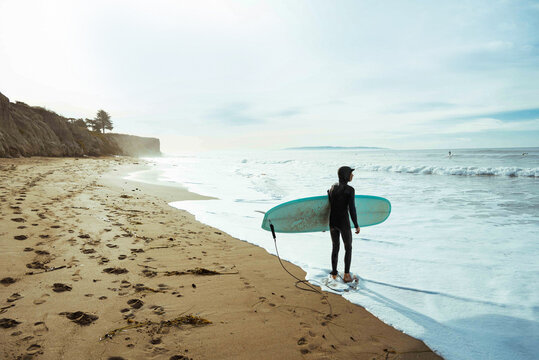 Surfer with surfboard on beach, Morro Bay, California, United States
