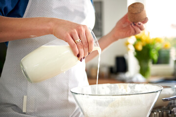 Woman pouring milk into mixing bowl in kitchen