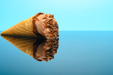 chocolate flavor ice cream cone starts melting on glass with reflection on blue background