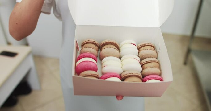 Close up box in hands of female confectioner. Traditional french dessert macaroons in a rows in paper present box. Colorful Macarons In A Gift Box In Hands Of Female Confectioner.