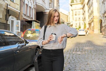 Obraz na płótnie Canvas Outdoor young business woman with paper cup of coffee looking at wrist watch