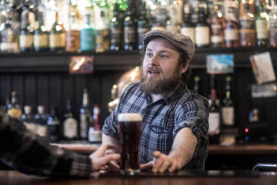 Barman serving beer to customer at bar in traditional Irish public house