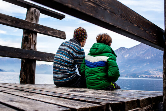Boy and father sitting on lakeside pier, rear view, Lake Como, Onno, Lombardy, Italy