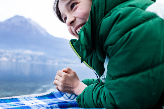 Boy in green anorak lying on picnic blanket by lakeside, cropped, Lake Como, Onno, Lombardy, Italy