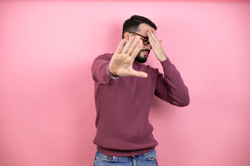Handsome man wearing glasses and casual clothes over pink background covering eyes with hands and doing stop gesture with sad and fear expression. Embarrassed and negative concept.