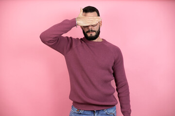 Handsome man wearing glasses and casual clothes over pink background serious and covering his eyes with his hand