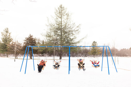 Man and children swinging on row of playground swings in snow