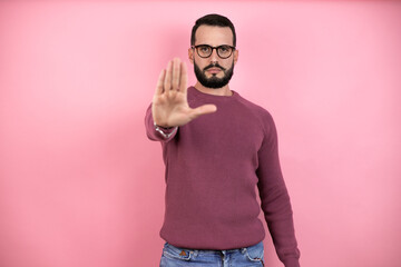 Handsome man wearing glasses and casual clothes over pink background serious and doing stop sing with palm of the hand.