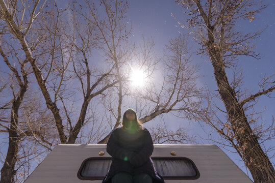 Woman beside campervan, bare trees in background