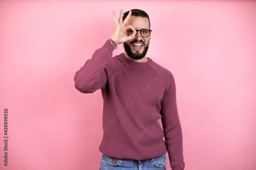 Canvas Prints Handsome man wearing glasses and casual clothes over pink background doing ok gesture shocked with smiling face, eye looking through fingers