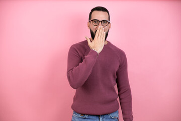 Handsome man wearing glasses and casual clothes over pink background covering mouth with hand, shocked and afraid for mistake. surprised expression