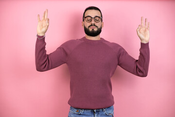 Handsome man wearing glasses and casual clothes over pink background relax and smiling with eyes closed doing meditation gesture with fingers