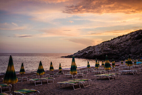 Rows of empty sun loungers and parasols on beach at sunset, Capoliveri, Tuscany, Italy