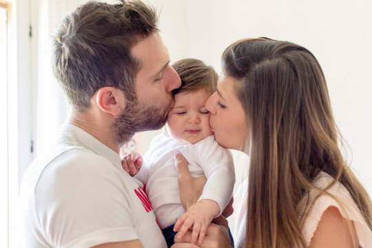 Parents kissing baby girl's cheeks at home