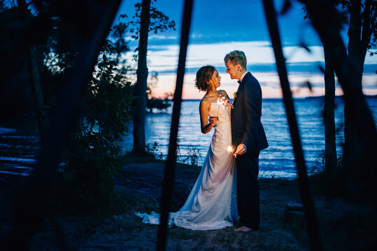Bride and groom with sparklers by lakeside at dusk, Lake Ontario, Toronto, Canada