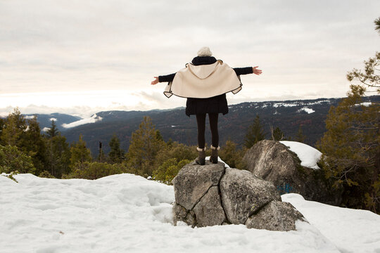 Young woman standing on rock on snow covered mountain, rear view, Twain Harte, California, USA