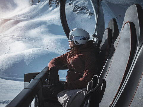 Young woman skier wearing helmet and ski goggles looking out from ski lift,  Alpe Ciamporino, Piemonte, Italy